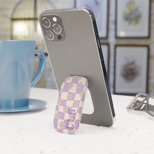 May include: A purple and white phone stand with a checkered pattern and yellow flowers. The stand has the letters "CLS" printed on it.