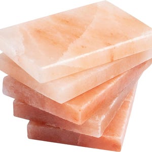 May include: A stack of five rectangular pink Himalayan salt slabs. The slabs are smooth and have a natural, slightly rough texture.