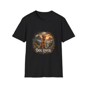 Peut inclure: Un t-shirt noir à manches courtes avec une impression graphique circulaire représentant un chien doré assis dans un paysage forestier avec des montagnes en arrière-plan. Sous le chien, le texte "DOG LOVER" est écrit en police serif.