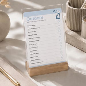 May include: A clear acrylic sign in a light wood base featuring a light blue header with the text Outdoor and a spray bottle icon. Below, a checklist includes tasks like Pick up rubbish, Sweep the patio, and Clean the door with circular checkboxes.