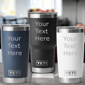 May include: Three insulated tumblers in navy blue, black, and white, each with a silver rim and the text "Your Text Here" engraved. The YETI logo is displayed at the bottom of each tumbler. These tumblers are designed to keep beverages cold or hot.