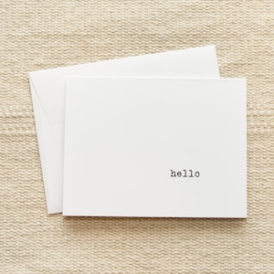 May include: A white card with a simple black font that reads "hello" on a beige textured background.