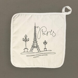May include: White cotton pot holder with a black line drawing of the Eiffel Tower, two street lamps, and the word "Paris" in cursive.
