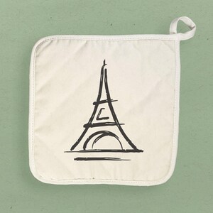 May include: White cotton pot holder with a black line drawing of the Eiffel Tower.