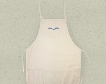May include: A plain white apron with a single pocket and a small blue floral design embroidered on the front.