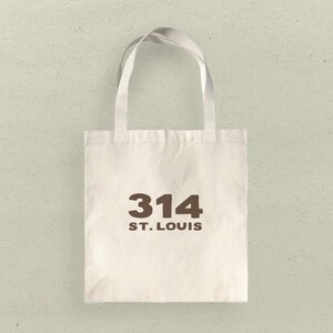 May include: A white canvas tote bag with brown text that reads "314 ST. LOUIS".