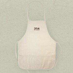 May include: A white canvas apron with a brown embroidered design that says "314 ST. LOUIS".