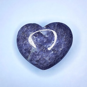 Puede incluir: Una piedra en forma de coraz&oacute;n en tonos azules y morados, con un dise&ntilde;o blanco curvado en su superficie. La piedra tiene un aspecto texturizado y est&aacute; sobre un fondo azul claro. Esta piedra decorativa podr&iacute;a usarse como pisapapeles o art&iacute;culo decorativo.