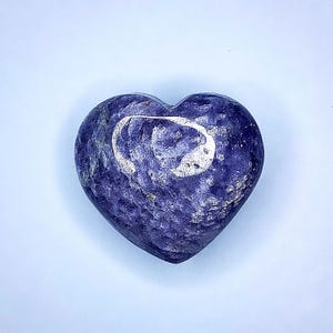 Puede incluir: Una piedra en forma de coraz&oacute;n de color azul oscuro, con un patr&oacute;n arremolinado y un dise&ntilde;o de media luna m&aacute;s claro y plateado. La piedra tiene una superficie texturizada y un fondo azul claro.
