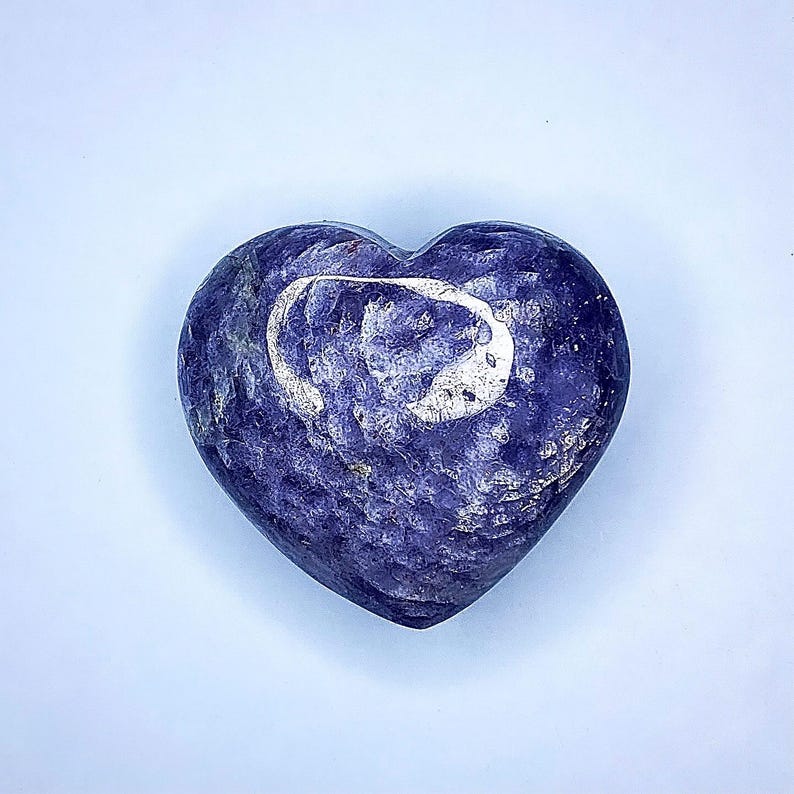 Puede incluir: Una piedra en forma de coraz&oacute;n de color azul oscuro, con un patr&oacute;n arremolinado y un dise&ntilde;o de media luna m&aacute;s claro y plateado. La piedra tiene una superficie texturizada y un fondo azul claro.