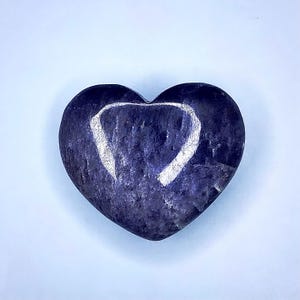 Puede incluir: Una piedra en forma de coraz&oacute;n en tonos azul oscuro y morado, con un dise&ntilde;o en forma de coraz&oacute;n blanco m&aacute;s claro grabado en su superficie. La piedra tiene un aspecto liso y pulido, sobre un fondo azul claro.