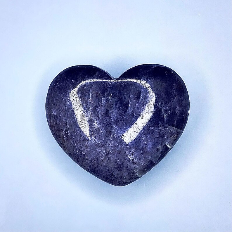 Puede incluir: Una piedra en forma de coraz&oacute;n en tonos azul oscuro y morado, con un dise&ntilde;o en forma de coraz&oacute;n blanco m&aacute;s claro grabado en su superficie. La piedra tiene un aspecto liso y pulido, sobre un fondo azul claro.