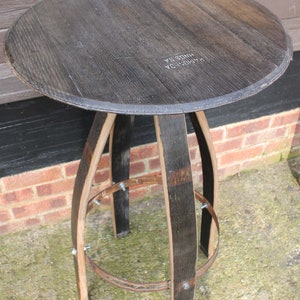 Peut inclure: Une table ronde en bois avec un plateau brun foncé et un piétement unique à trois pieds en fûts de vin récupérés. Le plateau de la table porte l'inscription "RAMSGEDA" et "HINDOS SA".