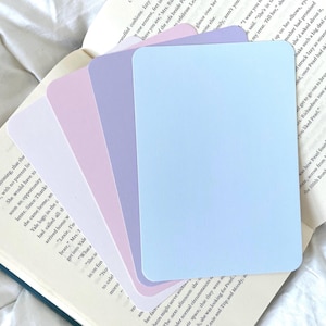 Puede incluir: Un juego de cinco tarjetas de índice en blanco en varios tonos de morado y azul, dispuestas de la más clara a la más oscura, sobre un libro abierto.