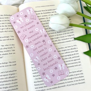 May include: Pink bookmark with a floral pattern and the text "no chance I'd waste my twenties on random men, not one of them is cooler than all my book boyfriends".