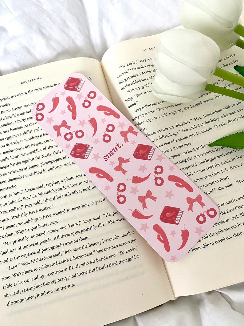 May include: A pink bookmark with a red book, handcuffs, chili peppers, and bows. The bookmark has the word "smut" printed on it.
