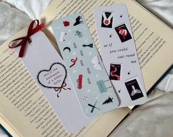 May include: Three decorative bookmarks with various designs. One bookmark has a heart with the text "this is the bookmark of a killer, Bella". Another has the text "as if you could out-read me". The third bookmark has various small illustrations.