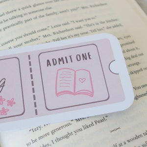 May include: A pink and white bookmark with the text "Membership Dating Club, right?" and "ADMIT ONE" with a pink open book illustration.