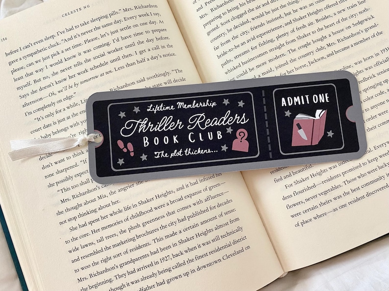 Op de afbeelding: Een grijs en zwart bladwijzer met een ticketontwerp. De bladwijzer bevat de tekst "Lifetime Membership Thriller Readers Book Club" en "The plot thickens..."  De bladwijzer heeft ook een rood-witte illustratie van een boek met een mes dat eruit steekt. De tekst "ADMIT ONE" staat op de bladwijzer gedrukt.