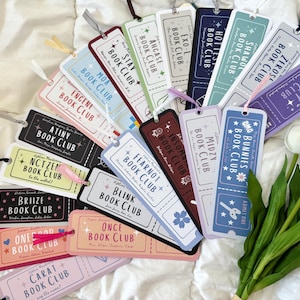 May include: A collection of rectangular paper bookmarks designed like admission tickets, each featuring a unique color, a specific fan club name, and a ribbon tassel. The bookmarks display text such as MOA, ENGENE, ATINY, NCTZEN, and CARAT BOOK CLUB.