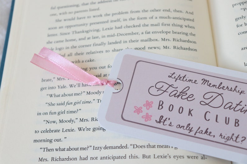 May include: A pink ribbon bookmark with the text "Lifetime Membership Fake Dating Book Club It's only fake, right?" printed on a white background with pink flowers.