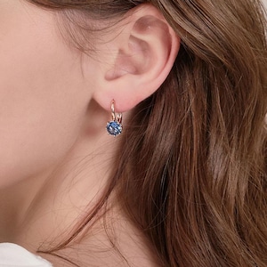 May include: A pair of rose gold hoop earrings with a blue gemstone in the center. The earrings are simple and elegant.