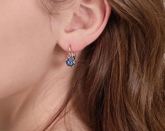 Puede incluir: Un par de pendientes de aro de oro rosa con una piedra preciosa azul en el centro. Los pendientes son simples y elegantes.