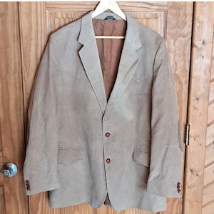 Puede incluir: Una chaqueta de pana beige con forro marrón, tres botones y parches en los codos. La chaqueta tiene un corte clásico y un cuello de punta.