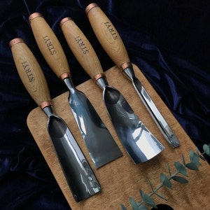 Puede incluir: Cuatro cinceles de mango de madera con hojas de metal. Los mangos están todos grabados con la palabra "STRYI". Los cinceles están dispuestos sobre una superficie de madera.