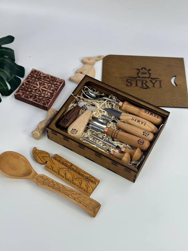 May include: A wooden box set containing carving tools and utensils, including a spoon, fork, and knife. The set includes a wooden stamp and a decorative wooden bunny. The box is branded with the word "STRYI".