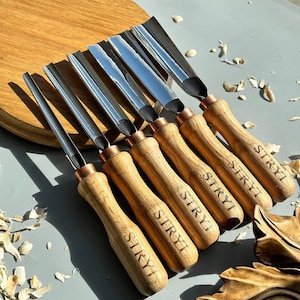 Pu&ograve; includere: Set di sette strumenti per intagliare il legno con manici in legno. Gli strumenti hanno una finitura argentata e sono etichettati "STRYI" sui manici.