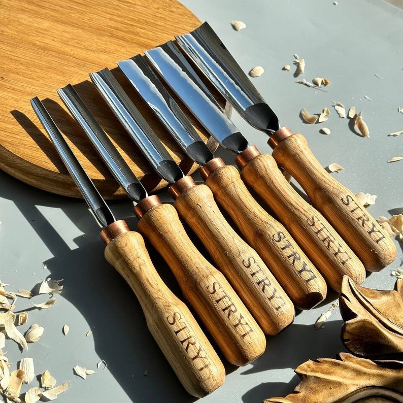 Pu&ograve; includere: Set di sette strumenti per intagliare il legno con manici in legno. Gli strumenti hanno una finitura argentata e sono etichettati "STRYI" sui manici.