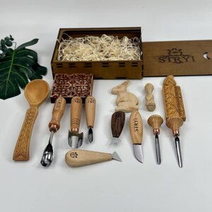 May include: A selection of wood carving tools and a wooden box with the text "STRYI". The tools include chisels, knives, and a spoon, all with wooden handles and metal blades. A carved wooden rabbit and other decorative wooden pieces are also included.