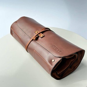 May include: A brown leather roll-up case with a strap and buckle closure. The case has the word "STRYI" embossed on the front.