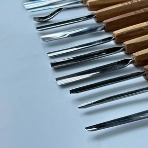 May include: A set of 12 wood carving tools with wooden handles. The tools have different shaped blades for carving wood.