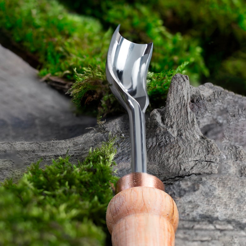 Pu&ograve; includere: Un primo piano di uno strumento per intagliare il legno con una lama in metallo e un manico in legno. Lo strumento &egrave; appoggiato su un letto di muschio verde.