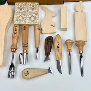 May include: A selection of wood carving tools and wooden shapes, including a rabbit, candle, and geometric tiles. The tools have wooden handles and metal blades. A wooden box with the word "STRYI" is in the background.