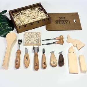 May include: A wood carving set featuring a selection of tools such as gouges, knives, and a spoon. The set includes a wooden box, and the brand name "STRYI" is visible on some tools. Wooden cutouts of a rabbit and other shapes are also included.