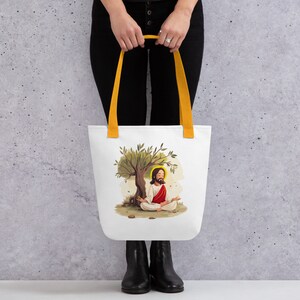 May include: White tote bag with yellow handles featuring a colorful illustration of Jesus meditating under an olive tree.
