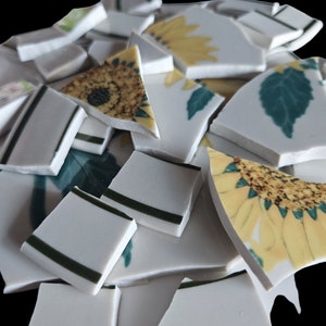 Könnte beinhalten: Ein Haufen zerbrochener weißer Keramikfliesen mit Sonnenblumen- und Blattmotiven. Die Fliesen sind in verschiedenen Formen und Größen zerbrochen.