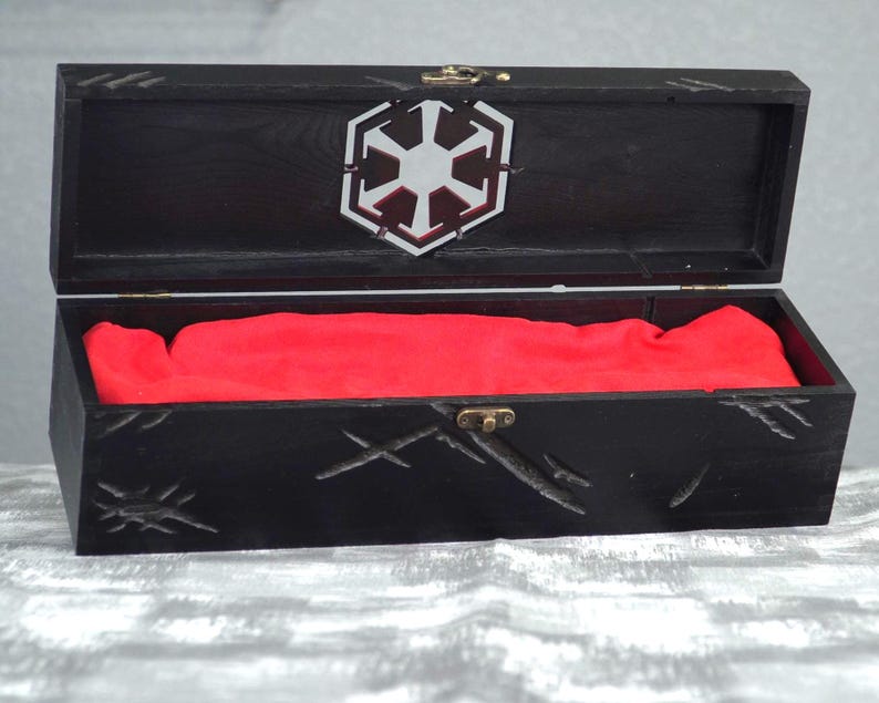 May include: Black wooden box with a hinged lid, featuring a silver emblem and red fabric lining. The box has carved details and a brass clasp. The open box reveals the red interior.