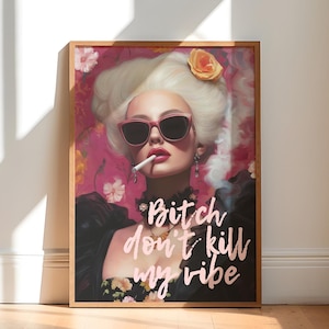 May include: A framed art print depicting a woman with white hair, sunglasses, and a cigarette, set against a pink floral backdrop. The print includes the text "Bitch don't kill my vibe". The frame is a light brown colour.