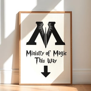 May include: A framed print with a black and white illustration of the Ministry of Magic symbol. The text "Ministry of Magic This Way" is below the symbol with a black arrow pointing down.