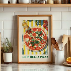 May include: A framed print featuring a pizza topped with tomato and basil. The pizza sits on a plate against a yellow and white striped backdrop. The text "CLUB DELLA PIZZA" is displayed at the bottom of the print.