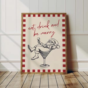 May include: A framed print featuring a relaxed Santa Claus figure holding a wine glass, reclining in a martini glass. The text "eat, drink and be merry" is written in red script. The print has a cream background with a red and white checkered border.