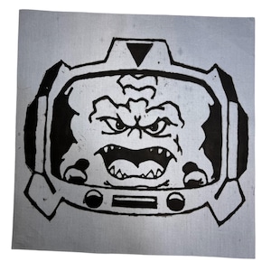 Puede incluir: Un grabado en linóleo en blanco y negro de un monstruo enojado con un casco. El monstruo tiene una sonrisa amplia y con dientes y el ceño fruncido. La impresión está sobre un fondo cuadrado gris claro.