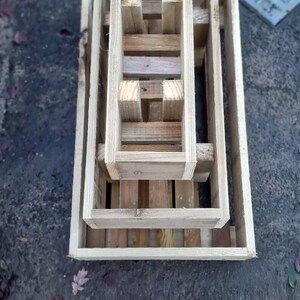 May include: Three unfinished wooden planters of varying sizes, stacked together. Each planter is rectangular with an open top and bottom, made from light-coloured wood. The planters are arranged in a nested design.