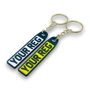 May include: Two black keychains with gold chains. One keychain has a white background with the text "YOUR REG" in black. The other keychain has a yellow background with the text "YOUR REG" in black.