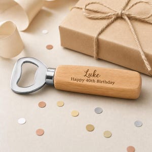 May include: A bottle opener with a light-toned wooden handle featuring the engraved text Luke Happy 40th Birthday. The metal head is silver-coloured and attached to the cylindrical wood grip, which is positioned near a wrapped gift box.