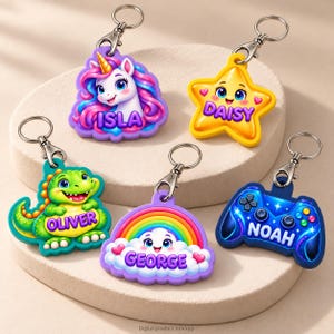Peut inclure: Cinq porte-clés colorés avec des fermoirs mousquetons en métal. Ils représentent une licorne nommée ISLA, une étoile jaune DAISY, un dinosaure vert OLIVER, un nuage arc-en-ciel GEORGE et une manette de jeu bleue nommée NOAH.